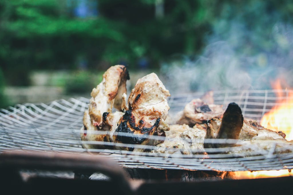 Juicy grilled meat cooking over charcoal flames outdoors, perfect for summer picnics and barbecues.